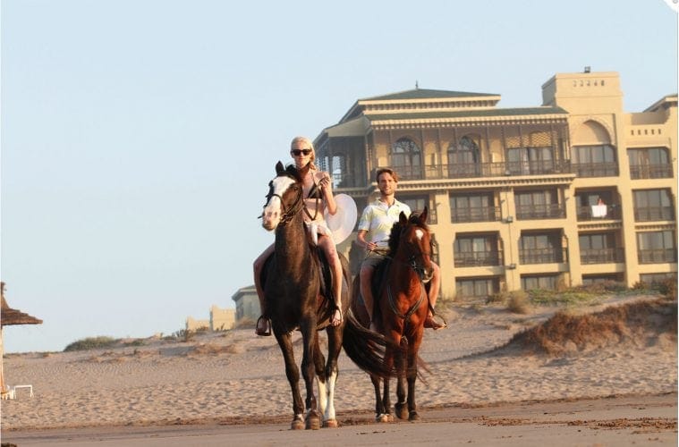 Touristen reiten auf Pferden am Strand des Mazagan Beach Resort