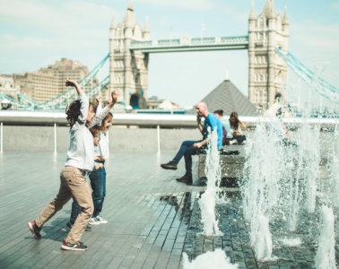Kinder in London spielen an öffentlichem Wasserstrahl vor der Tower Bridge