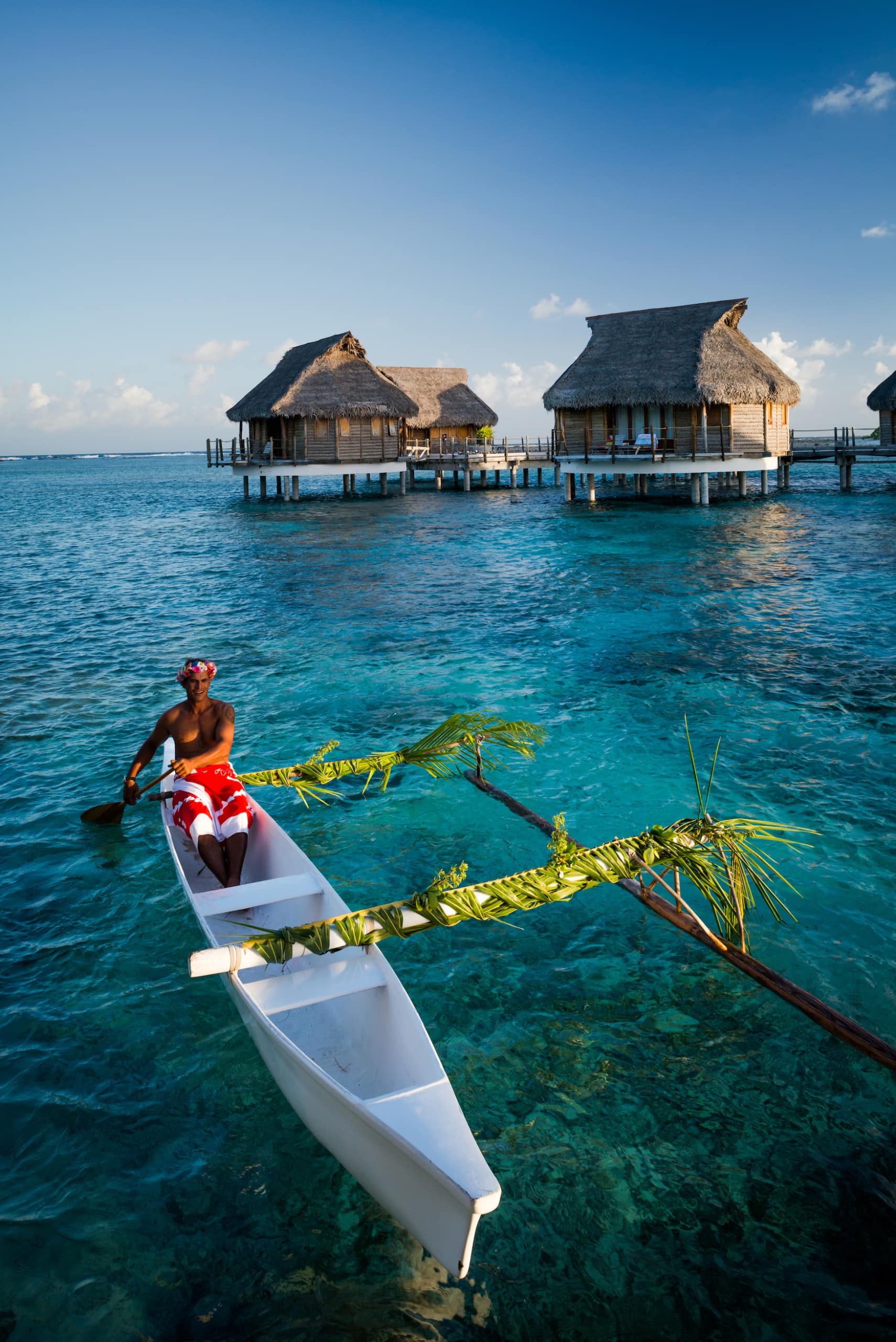 Polynesier paddelt auf Boot vor Überwasser-Bungalows in der Südsee