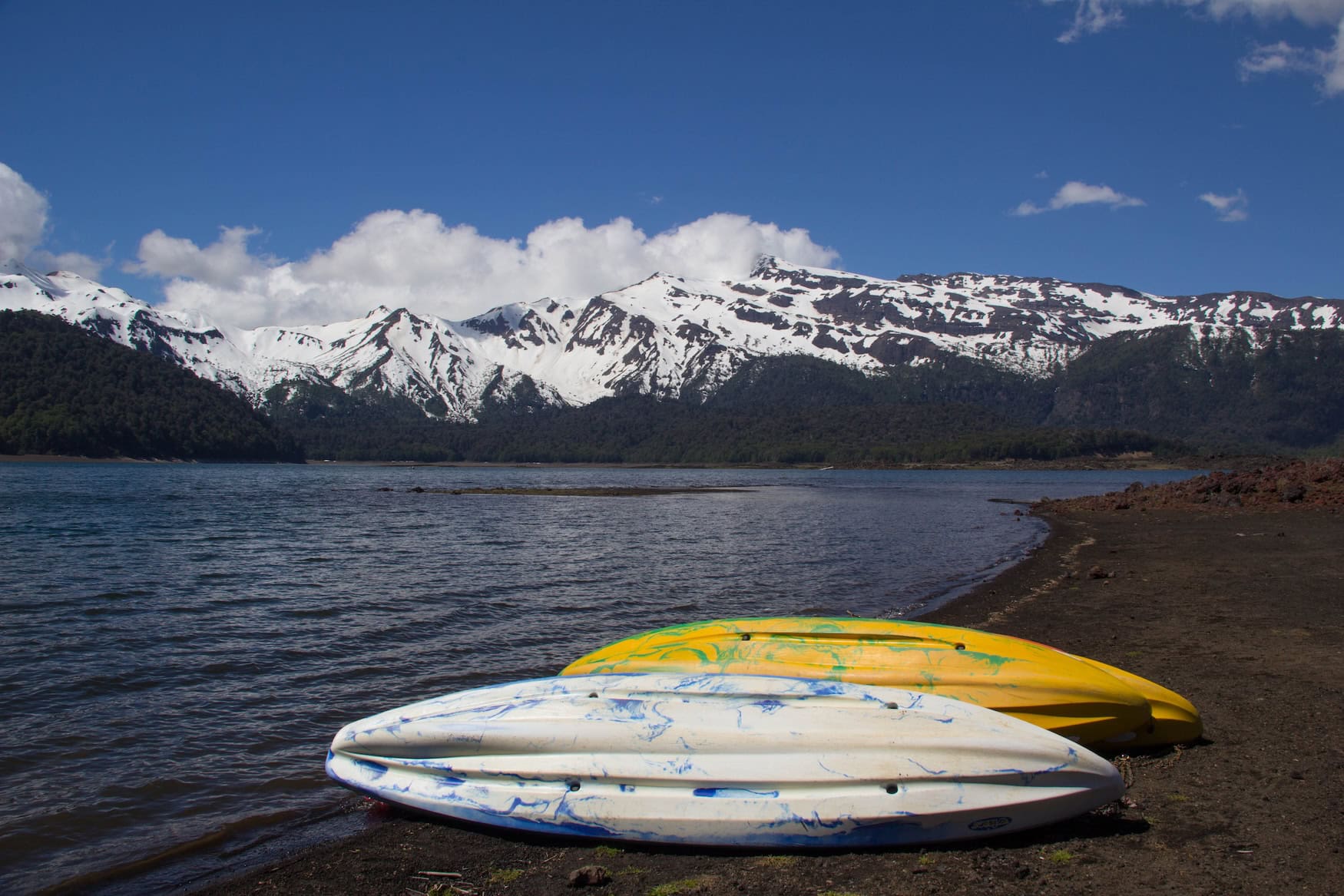 Kajaks am Ufer des Lago Conguillío vor der verschneiten Sierra Nevada im Nationalpark Conguillío, Chile.