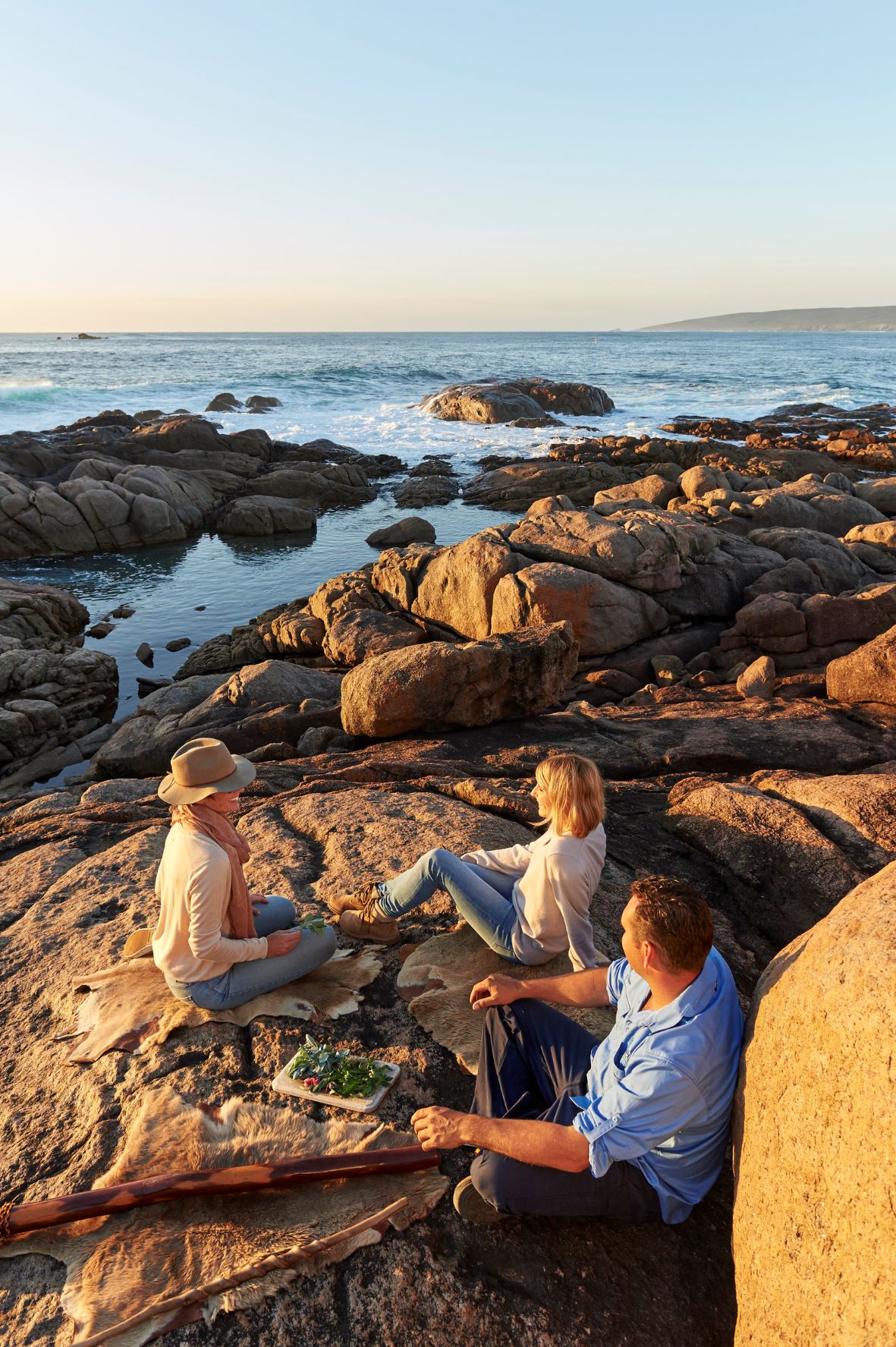 Touranbieter John Whiteland sitzt mit zwei Frauen auf Felsen am Meer 