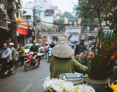 Frau mit Reishut schiebt ihr Fahrrad durch Straßen von Hanoi