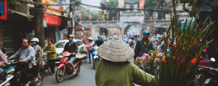 Frau mit Reishut schiebt ihr Fahrrad durch Straßen von Hanoi
