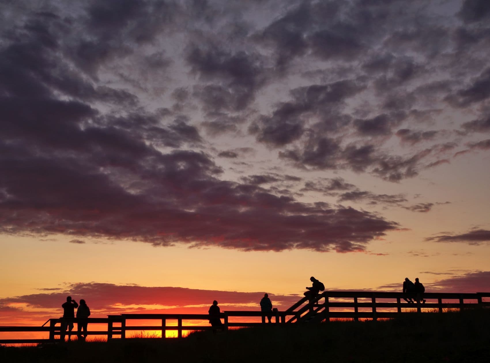 Menschen am Holzsteg während des Sonnenuntergangs auf Sylt 