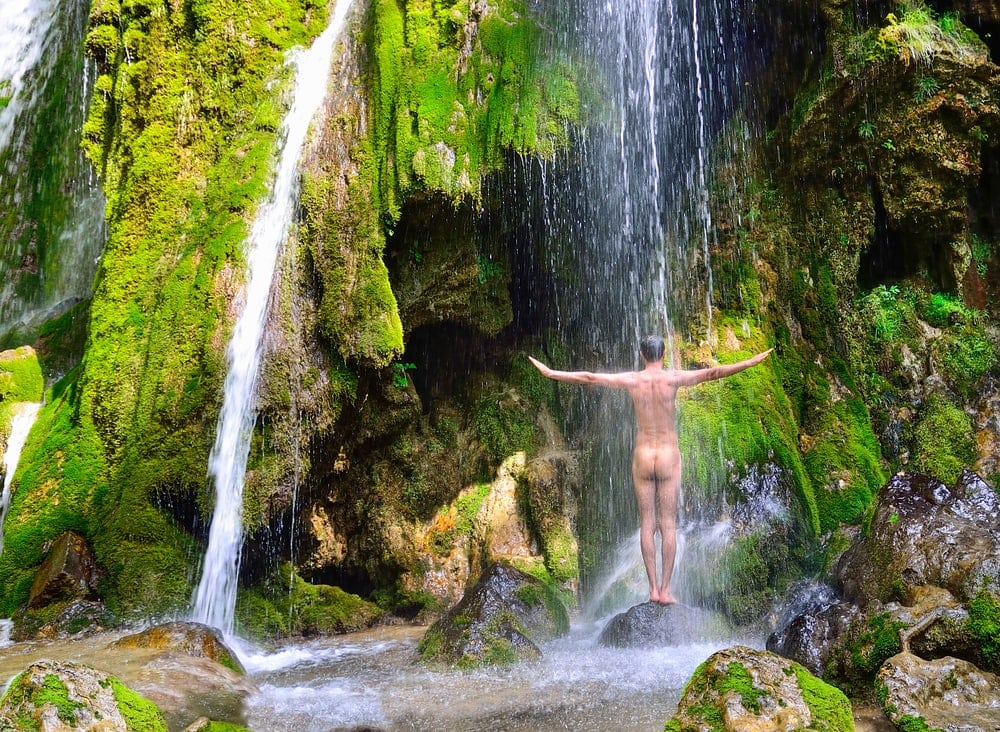 Nackturlaub: Ein Mann steht nackt unter einem Wasserfall 