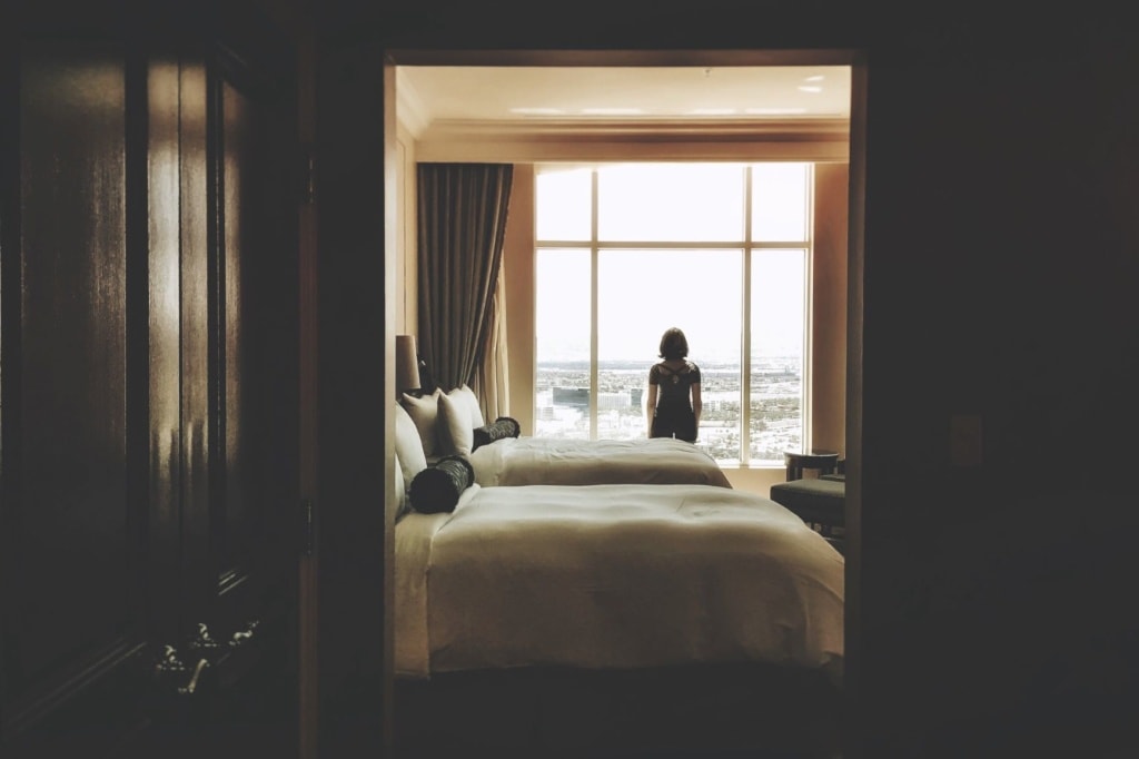 Frau steht im Hotelzimmer am Fenster und blickt hinaus 