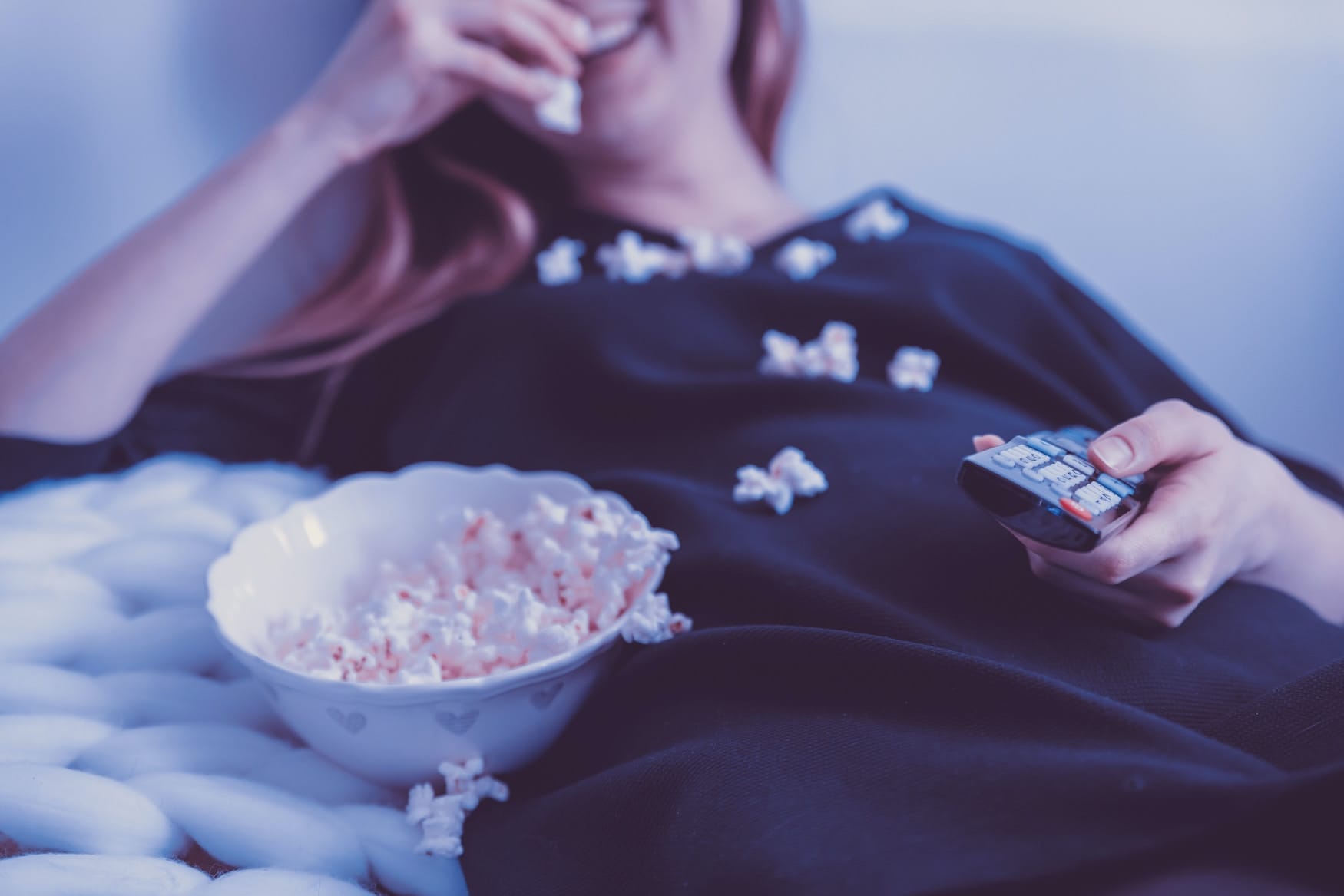Frau sitzt mit Popcorn vorm Fernseher