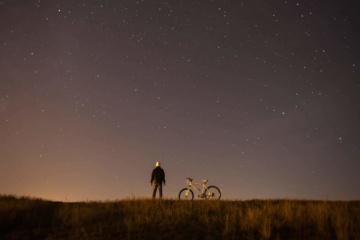 Mann mit Fahrrad blickt in Sternenhimmel