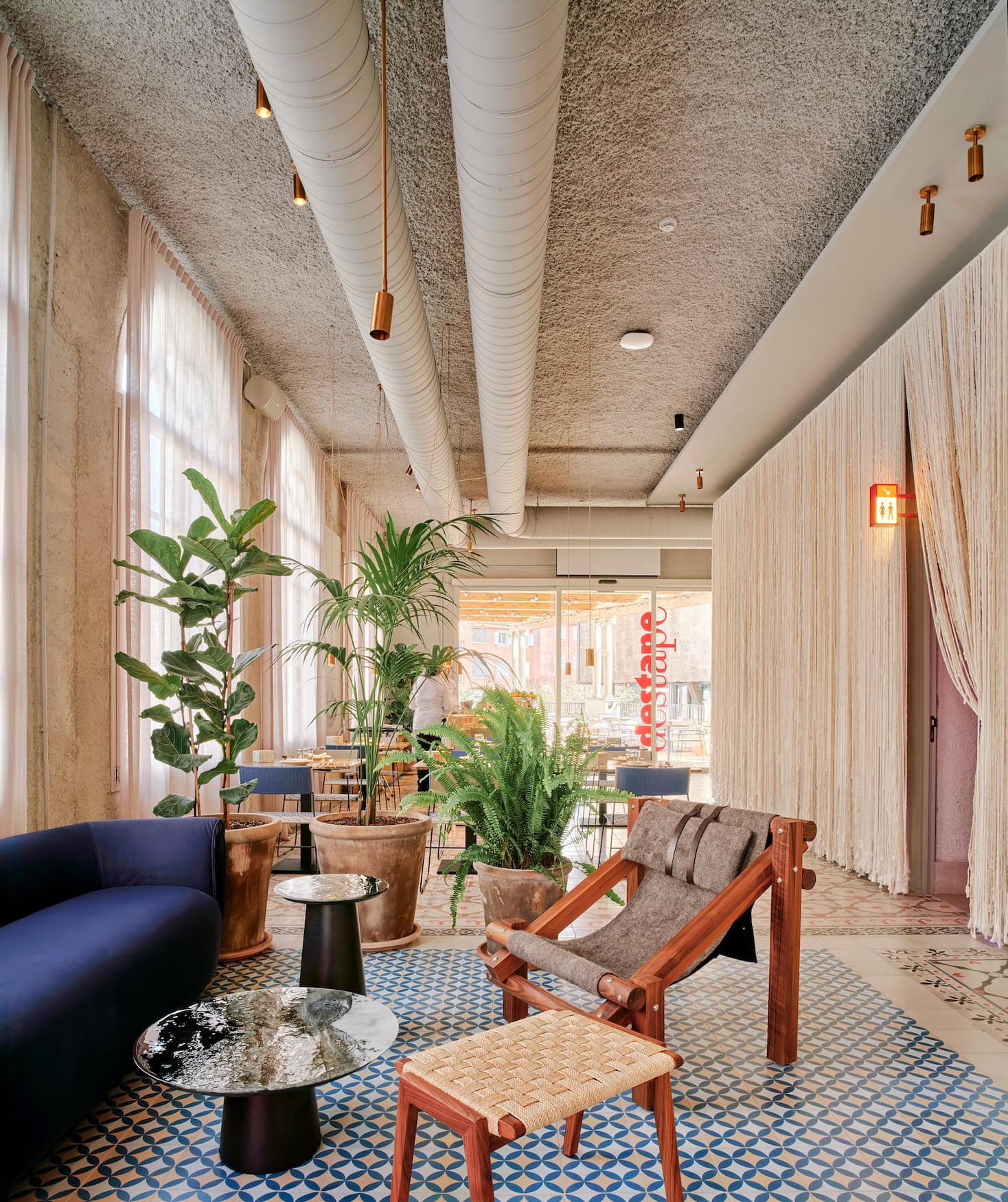 Lounge im Terreno Barrio Hotel mit blauem Sofa, Zementfliesen und Blick ins Restaurant Destape