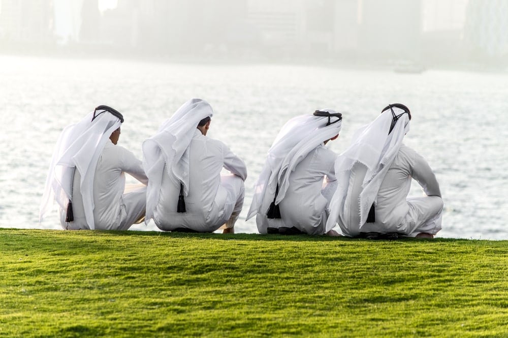 Männer in Katar, sitzend am Seeufer. Im Vordergrund eine grüne Wiese.