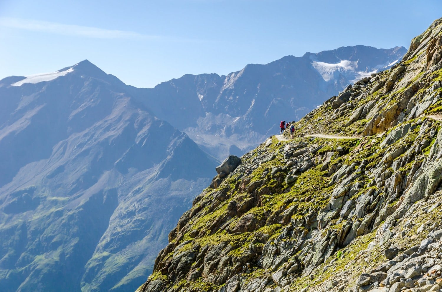 Wanderer auf einem schmalen Höhenweg am Fernwanderweg E5 vor vergletscherten Gipfeln der Ötztaler Alpen