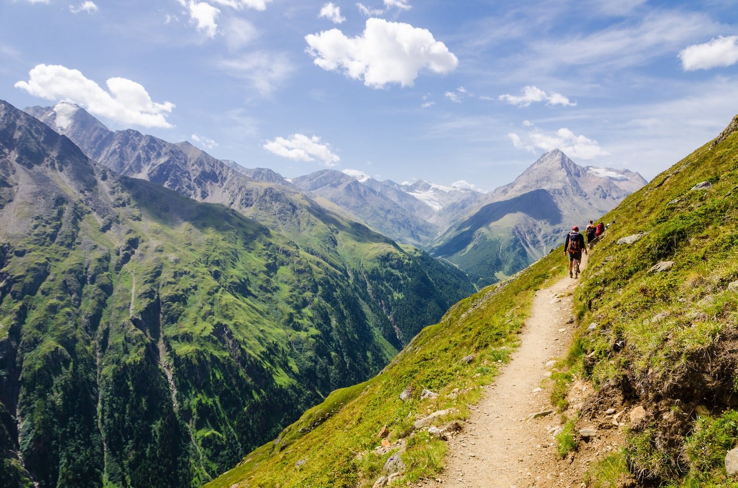 Wandergruppe auf einem Bergpfad des Fernwanderwegs E5 mit Blick in ein Tiroler Hochtal und auf Gletscher