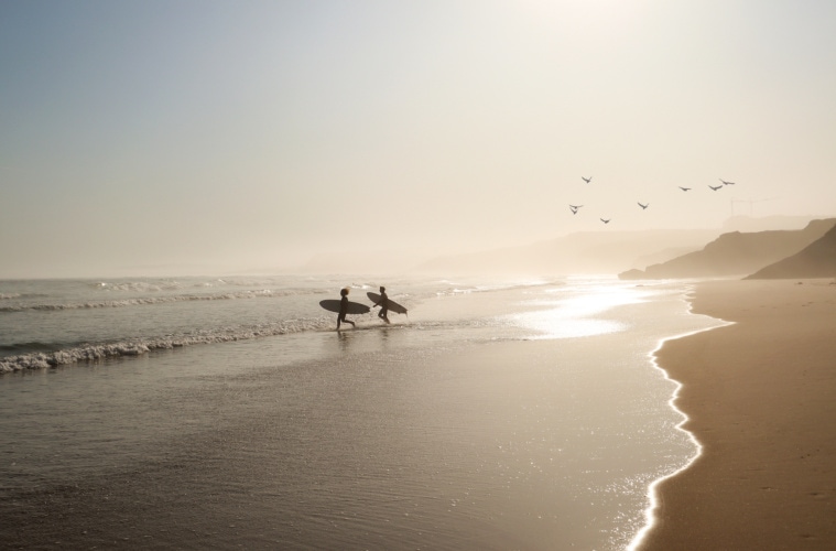 Surfer im Surfurlaub an einem Strand in Portugal während Sonnenuntergang