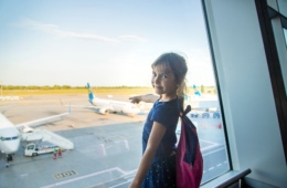 Junges Mädchen fliegt das erste Mal alleine und deutet mit Finger auf das Flugzeug