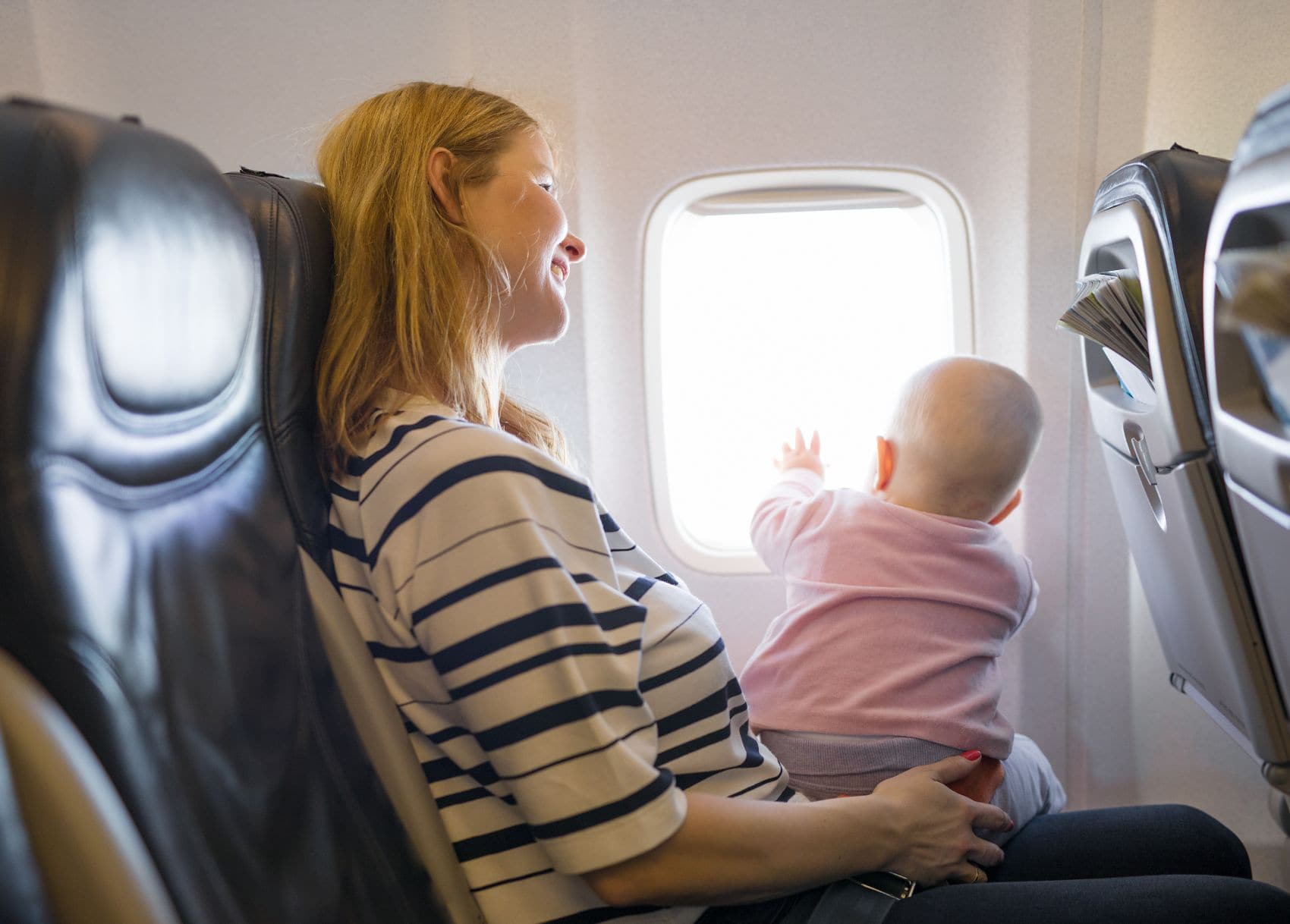 Mutter sitzt mit Baby im Flugzeug am Fenster