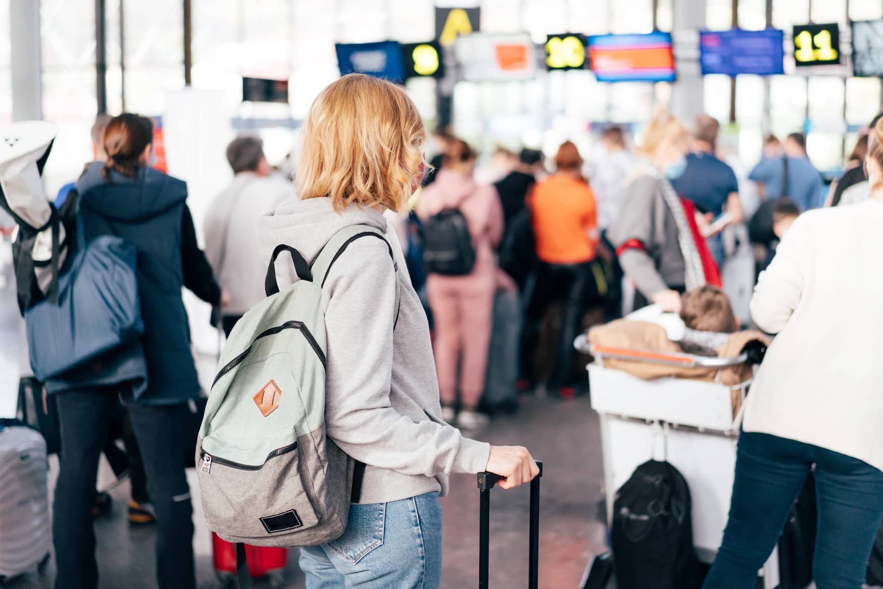 Junge Frau mit Rucksack steht vor der Warteschlange am Check-in-Schalter am Flughafen