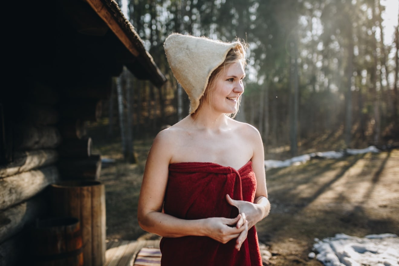 Frau mit Hut und rotem Handtuch kommt aus Sauna