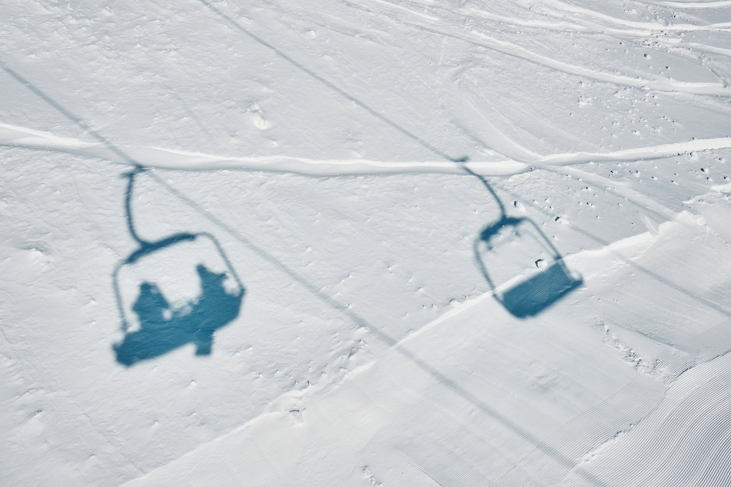 Schatten eines Sessellifts mit zwei Skifahrern auf einer verschneiten Skipiste