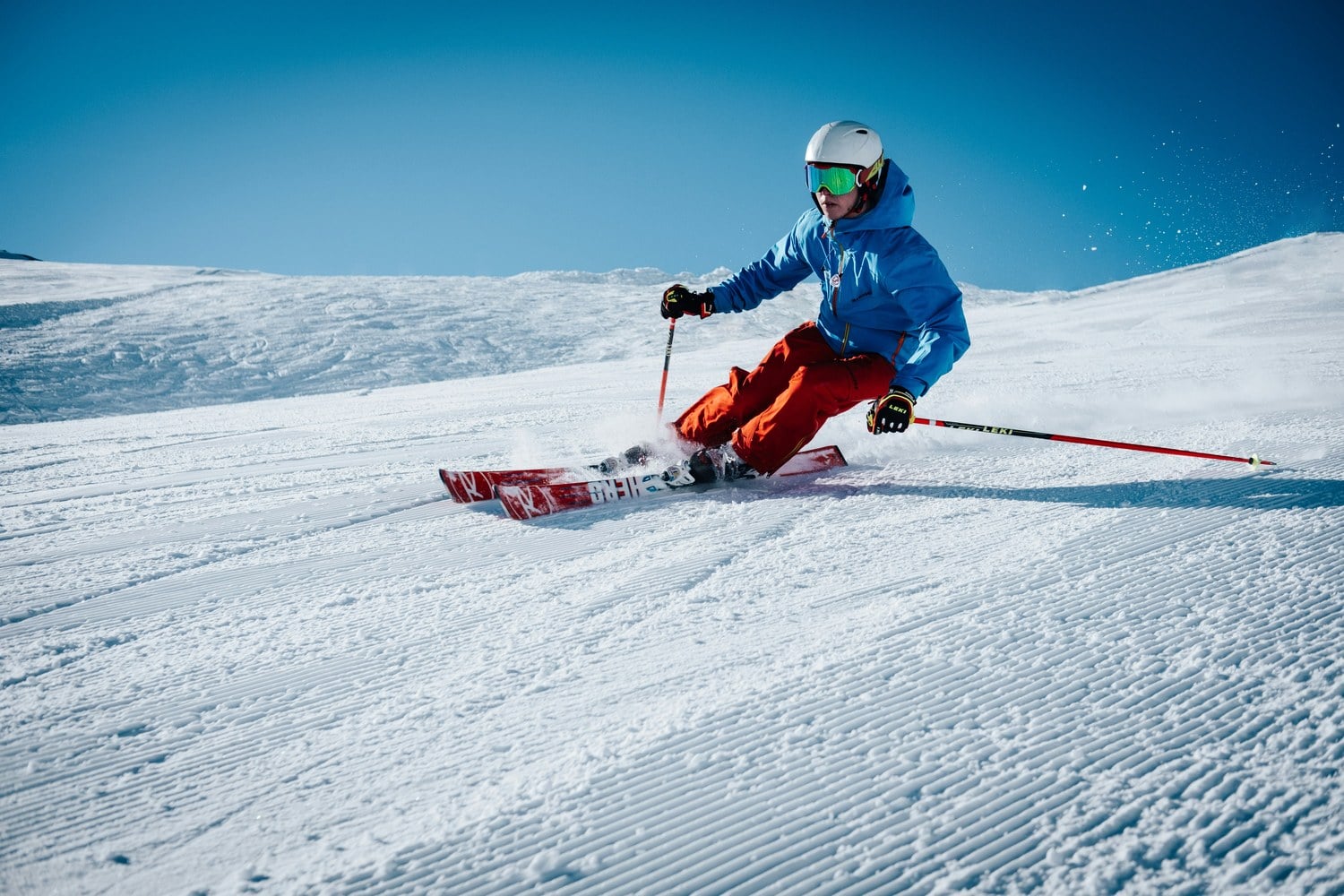 Skifahrer in blauer Jacke fährt bei Sonnenschein einen Carvingschwung auf frisch präparierter Piste