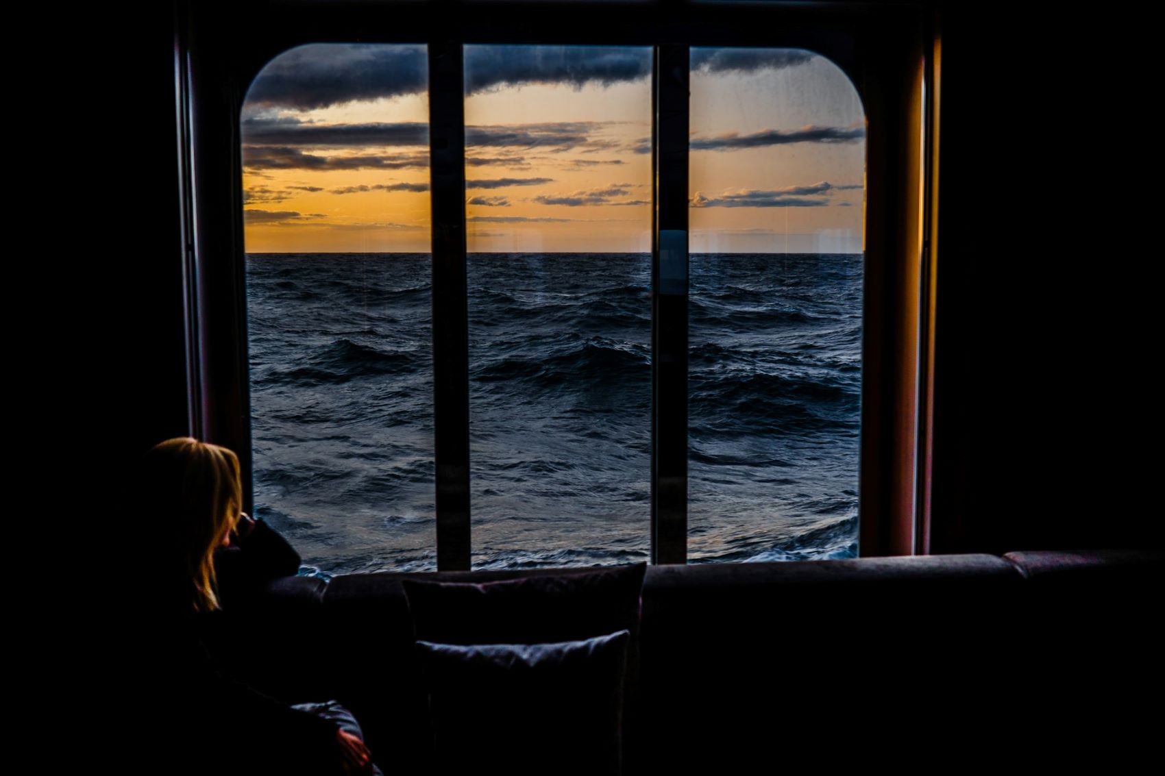 Frau sitzt an Fenster auf Schiff und blickt aufs Meer
