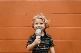Ein kleiner Junge steht vor einer orangefarbenen Wand und schleckt ein Eis.