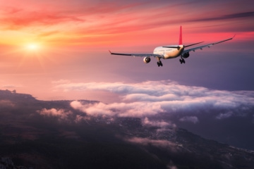 Flugzeug im roten Sonnenuntergang über Wolken und Meer
