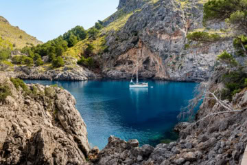 Eine idyllische Felsenbucht am Cala de Sa Calobra auf Mallorca, in der ein einzelnes Segelboot schwimmt.