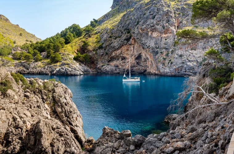 Eine idyllische Felsenbucht am Cala de Sa Calobra auf Mallorca, in der ein einzelnes Segelboot schwimmt.