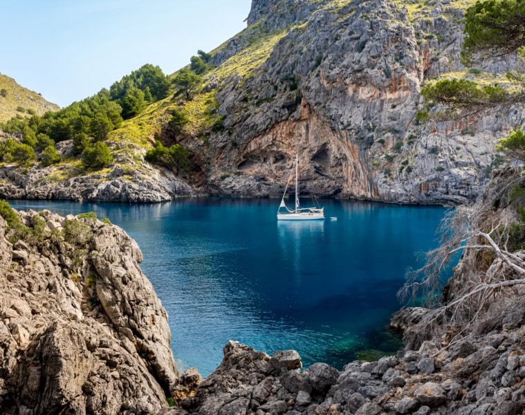 Eine idyllische Felsenbucht am Cala de Sa Calobra auf Mallorca, in der ein einzelnes Segelboot schwimmt.