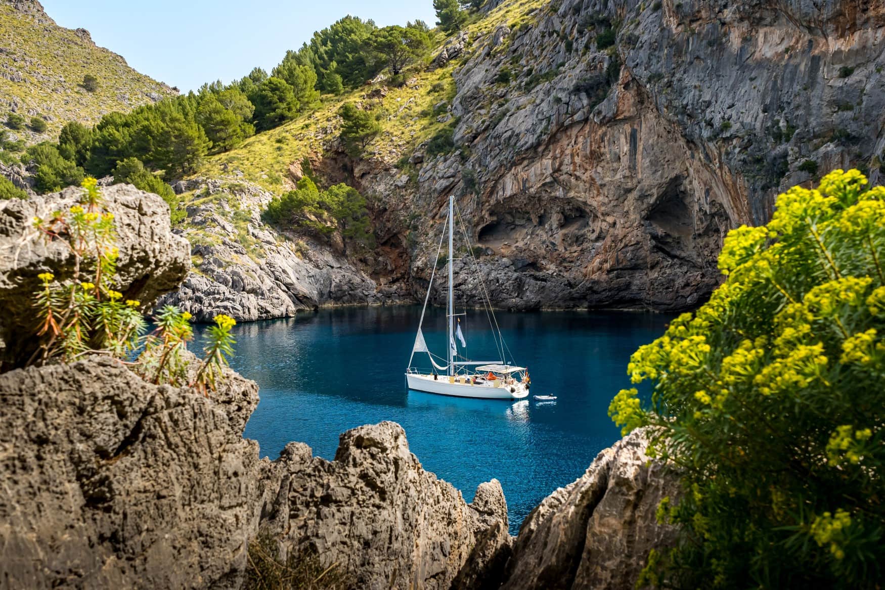 Eine idyllische Felsenbucht am Cala de Sa Calobra auf Mallorca, in der ein einzelnes Segelboot schwimmt.