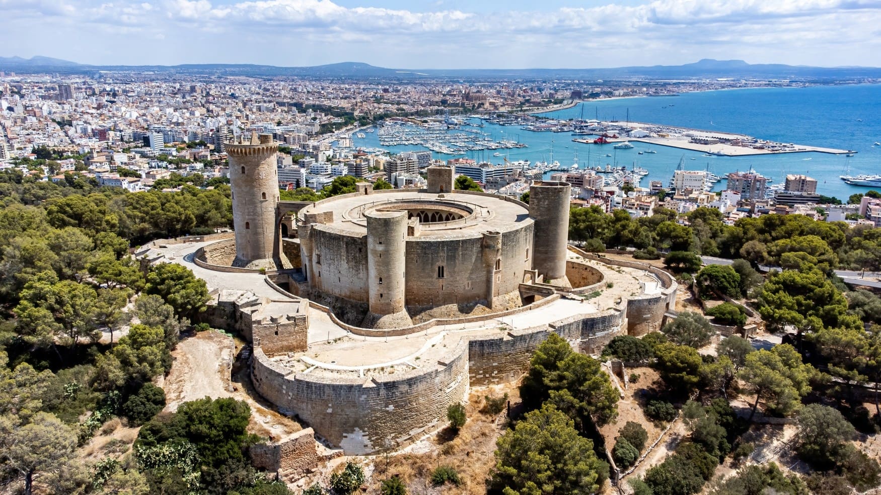 Luftaufnahme des Castell de Bellver auf Mallorca, eine kreisrunde Burg, die nochmals von einem eckigen Festungswall umgeben ist.