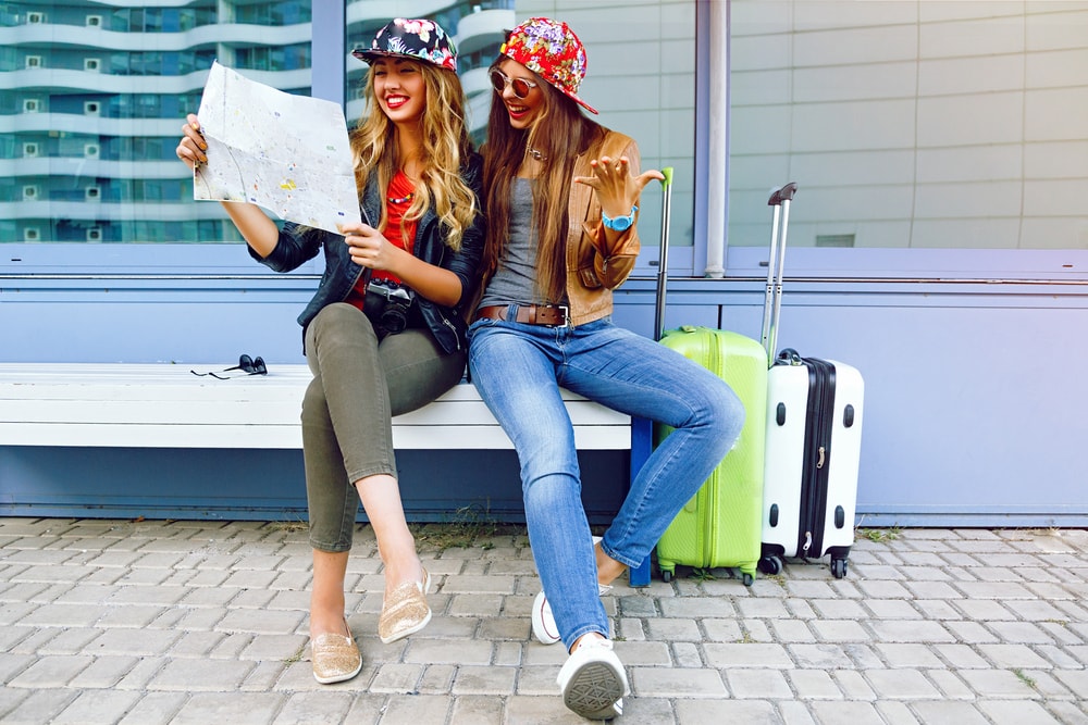 Zwei junge Damen mit Karte und Koffern