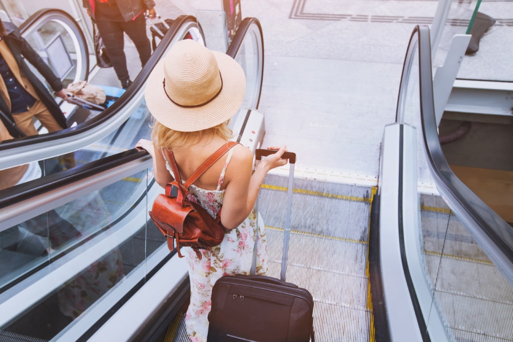 Frau mit Gepäck auf einer Rolltreppe im Flughafen