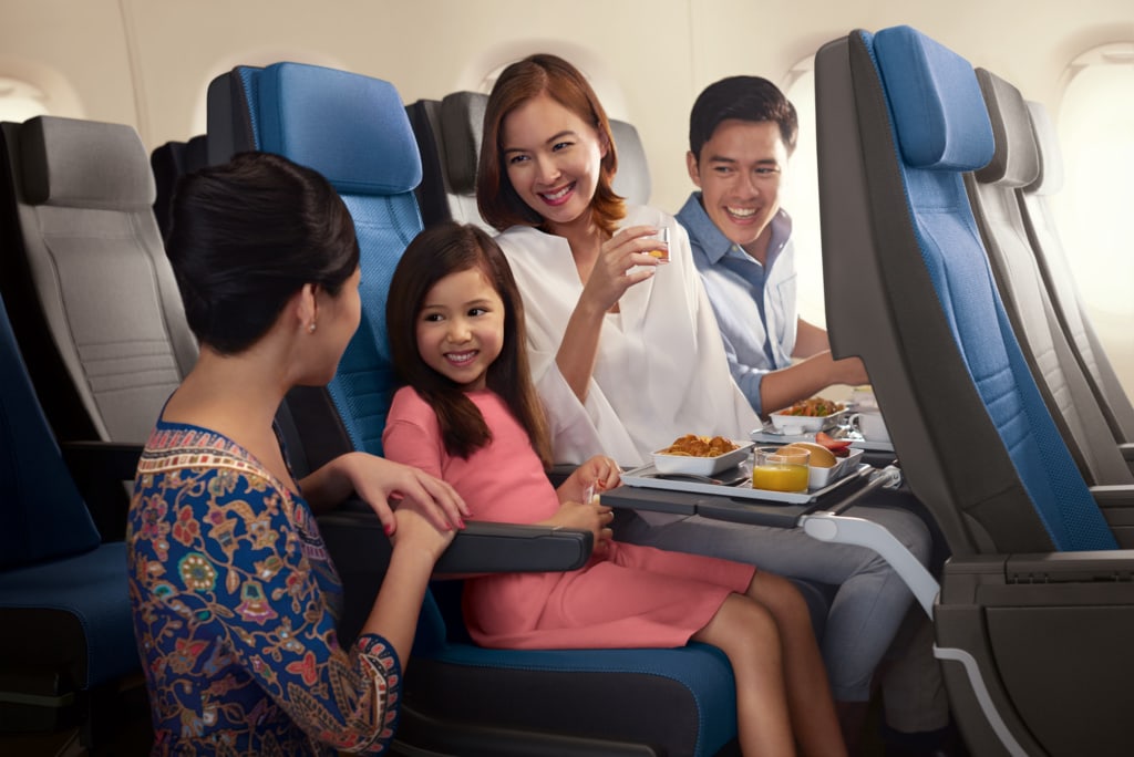 Singapore Girl kniet vor Familie in der Economy Class