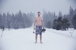 Mann steht halbnackt mit Sauna-Utensilien in finnischer Winterlandschaft