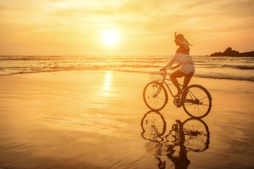 Frau fährt Fahrrad bei Sonnenuntergang am Strand