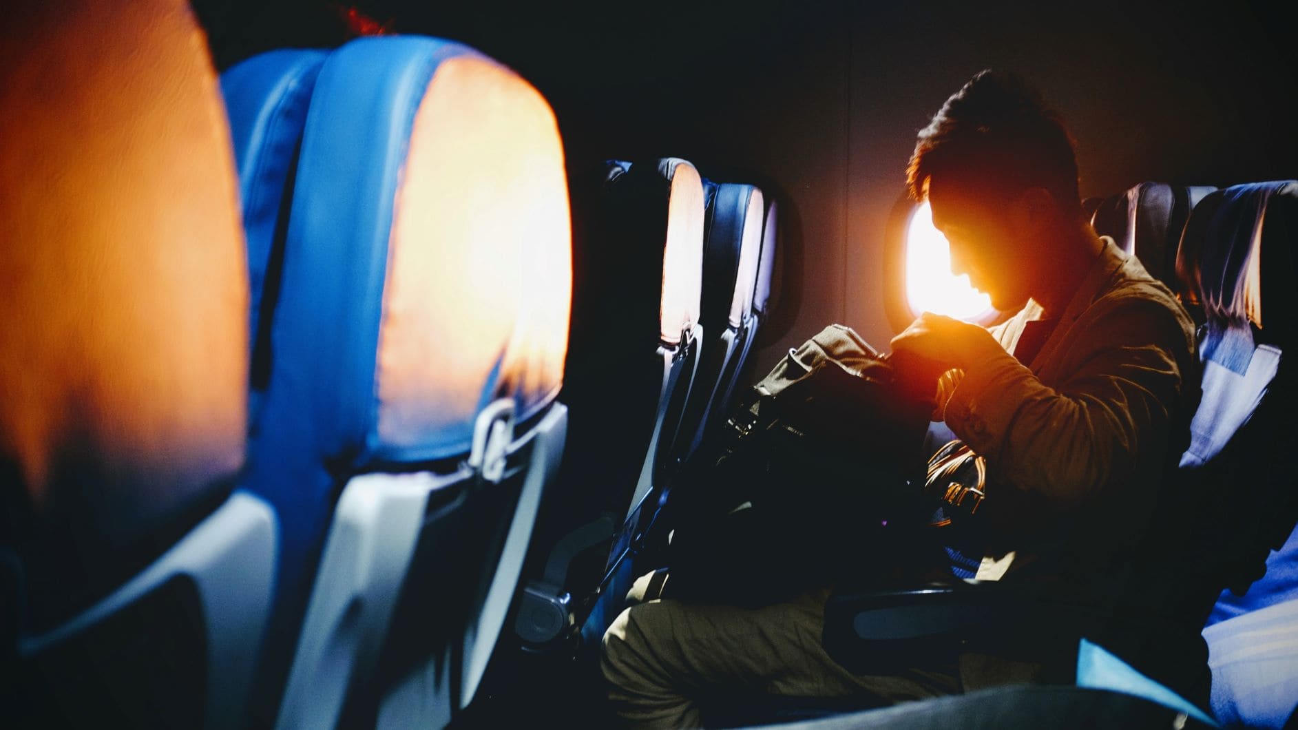 Mann sitzt im Flugzeug und durchsucht seinen Rucksack