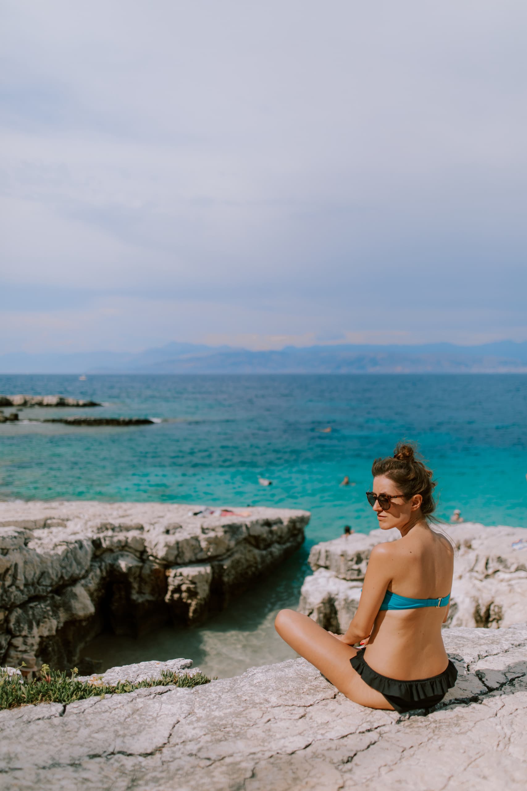 Frau sitzt im Bikini in griechischer Bucht und sonnt sich