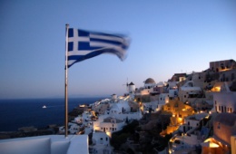 Griechische Flagge weht im Wind vor der Kulisse einer griechischen Insel bei Nacht