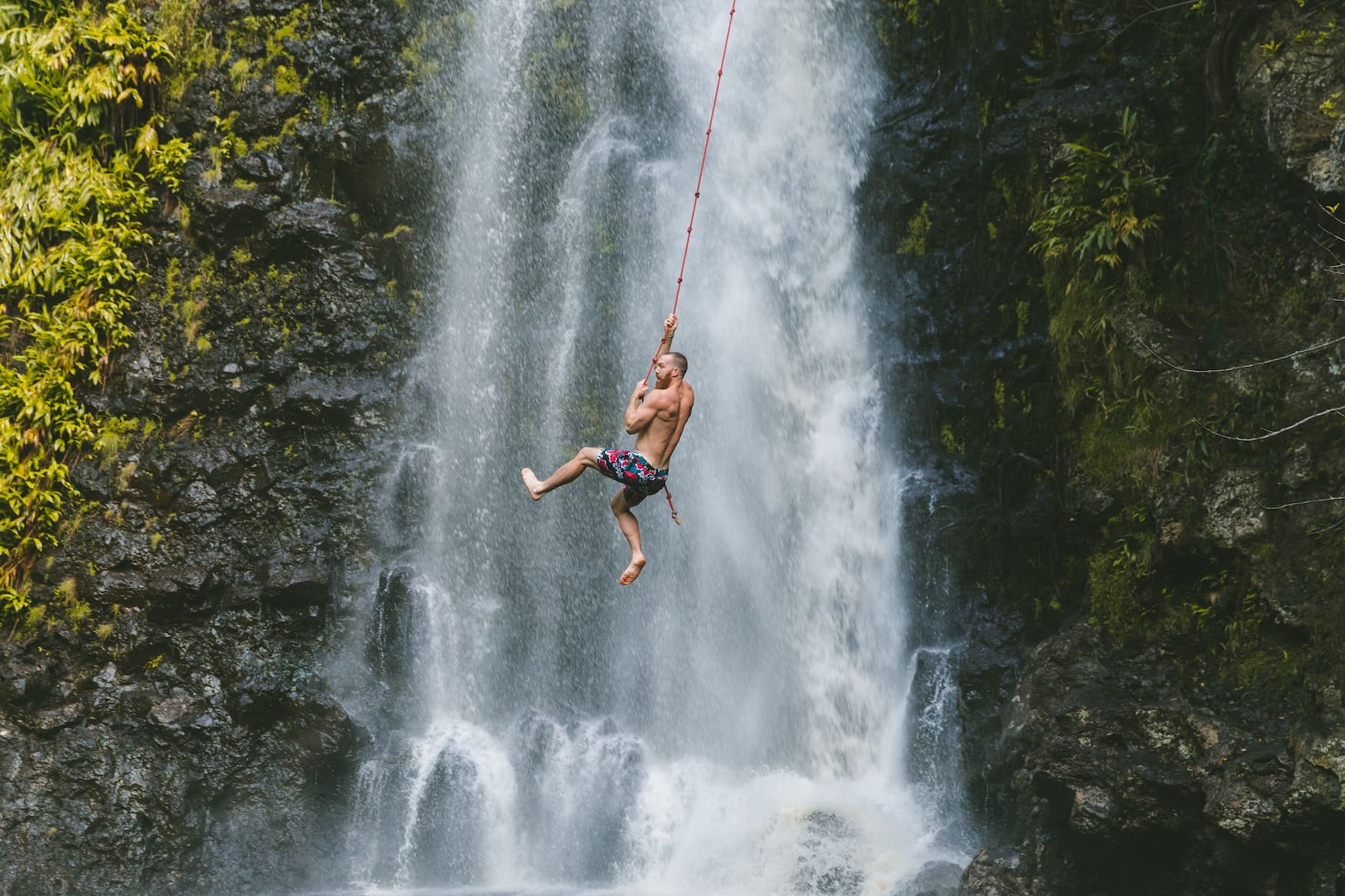 Mann schwingt auf Liane vor Wasserfall