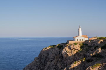Weißer Leuchtturm Far de Capdepera mit angebautem Wohngebäude auf einer Felsklippe über dem Mittelmeer bei Cala Ratjada.