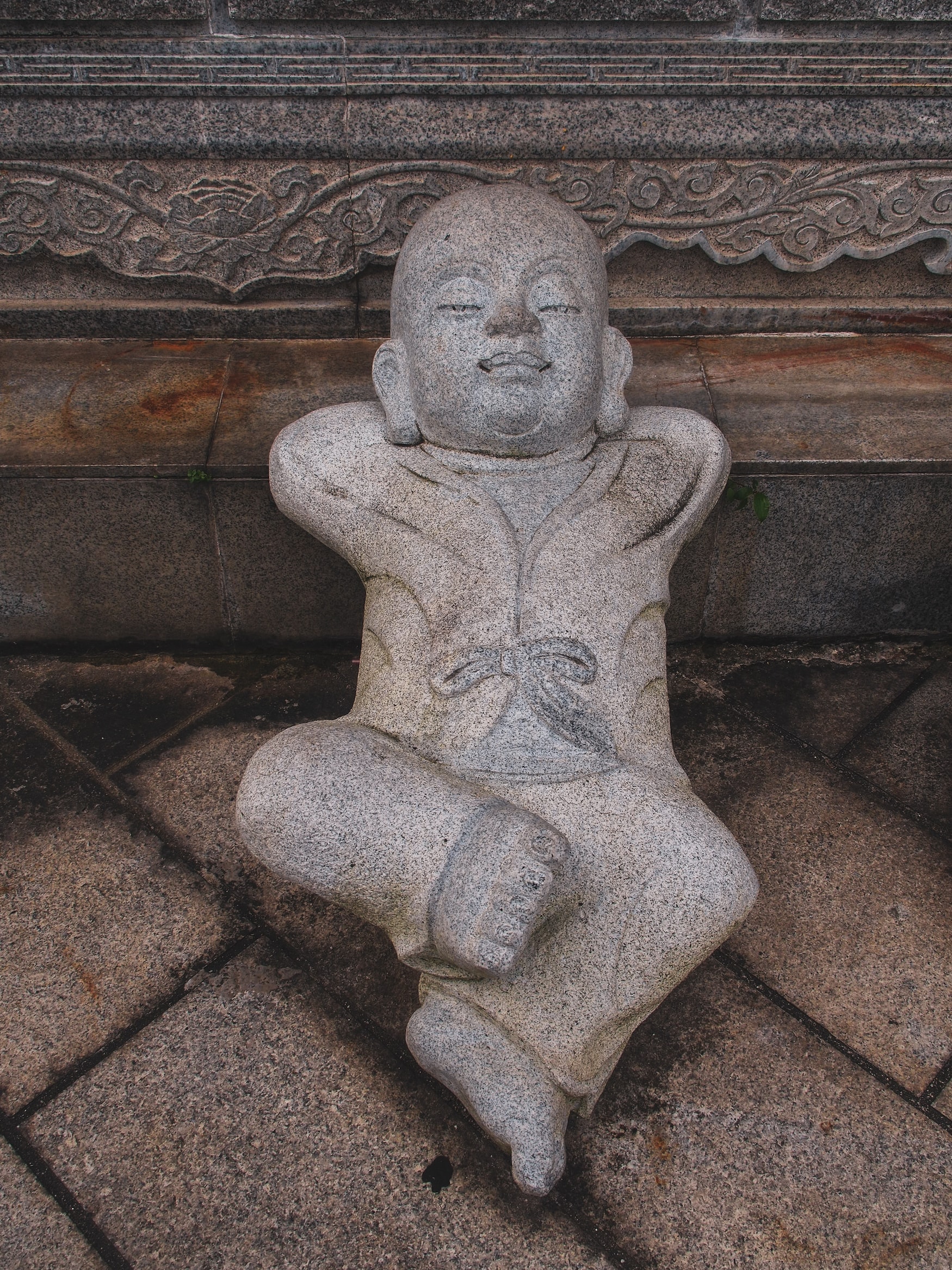 Kleine Buddha-Statue aus Stein liegt auf dem Rücken und verschränkt die Arme hinter dem Kopf