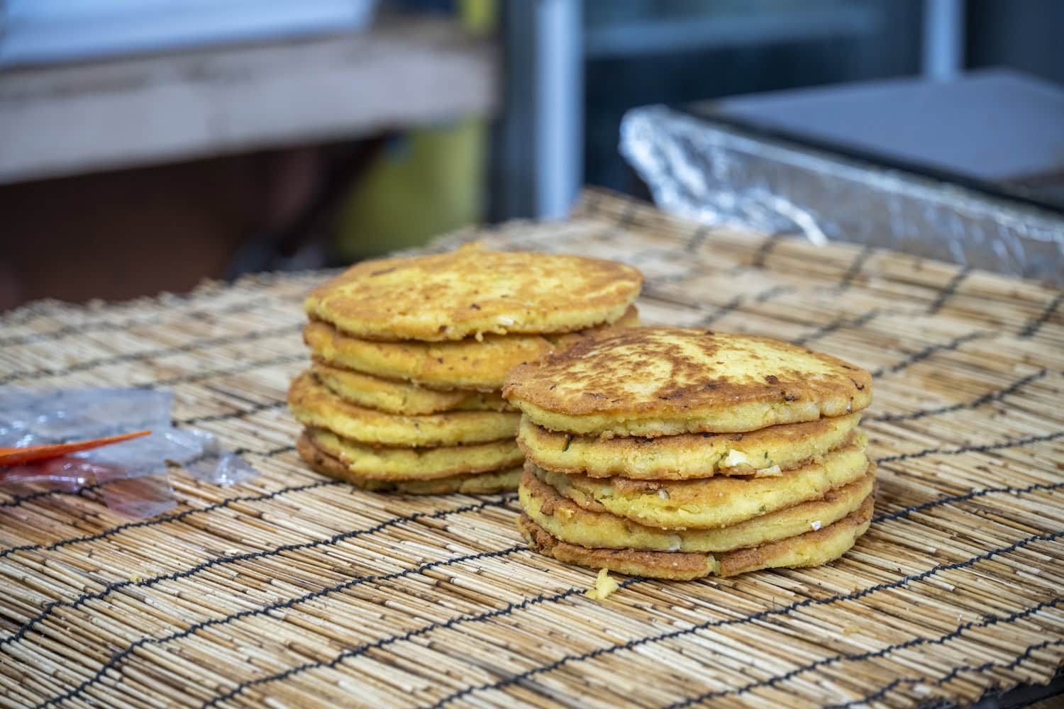 Knusprige Mungbohnen-Pfannkuchen (Bindaetteok), gestapelt auf einer Bambusmatte, an einem Stand auf einem traditionellen Fünftagemarkt in Südkorea.