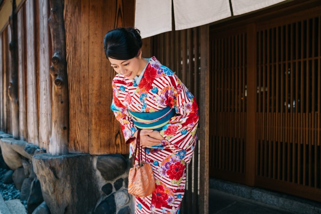Japanische Dame, die sich vor ihrem Haus mit einem Kimono bowing