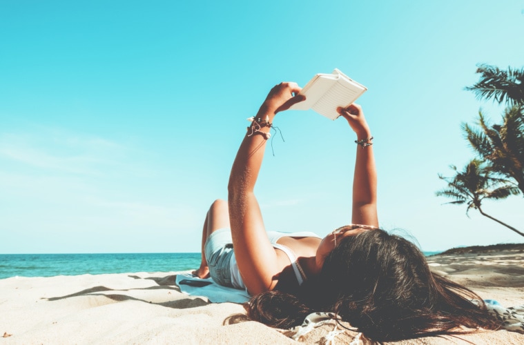 Mädchen liegt am Strand und liest ein Buch