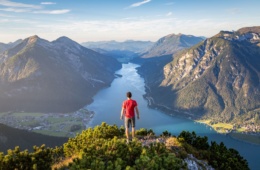 Mann blickt von Hügel auf Alpen und See in Österreich