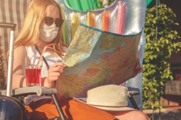 Frau im Liegestuhl mit Corona-Mund-Nasen-Maske und einer Landkarte in der Hand
