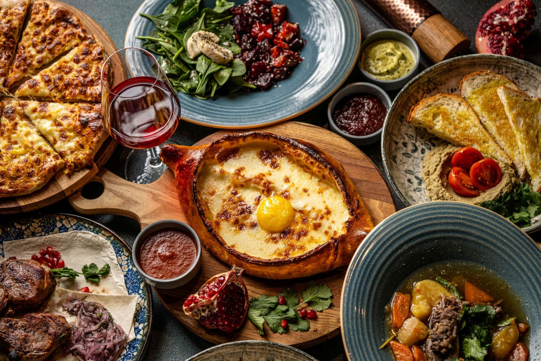 Eine reich gefüllte georgische Festtafel mit vielen Speisen, mittig ein mit Ei gefülltes Khachapuri.