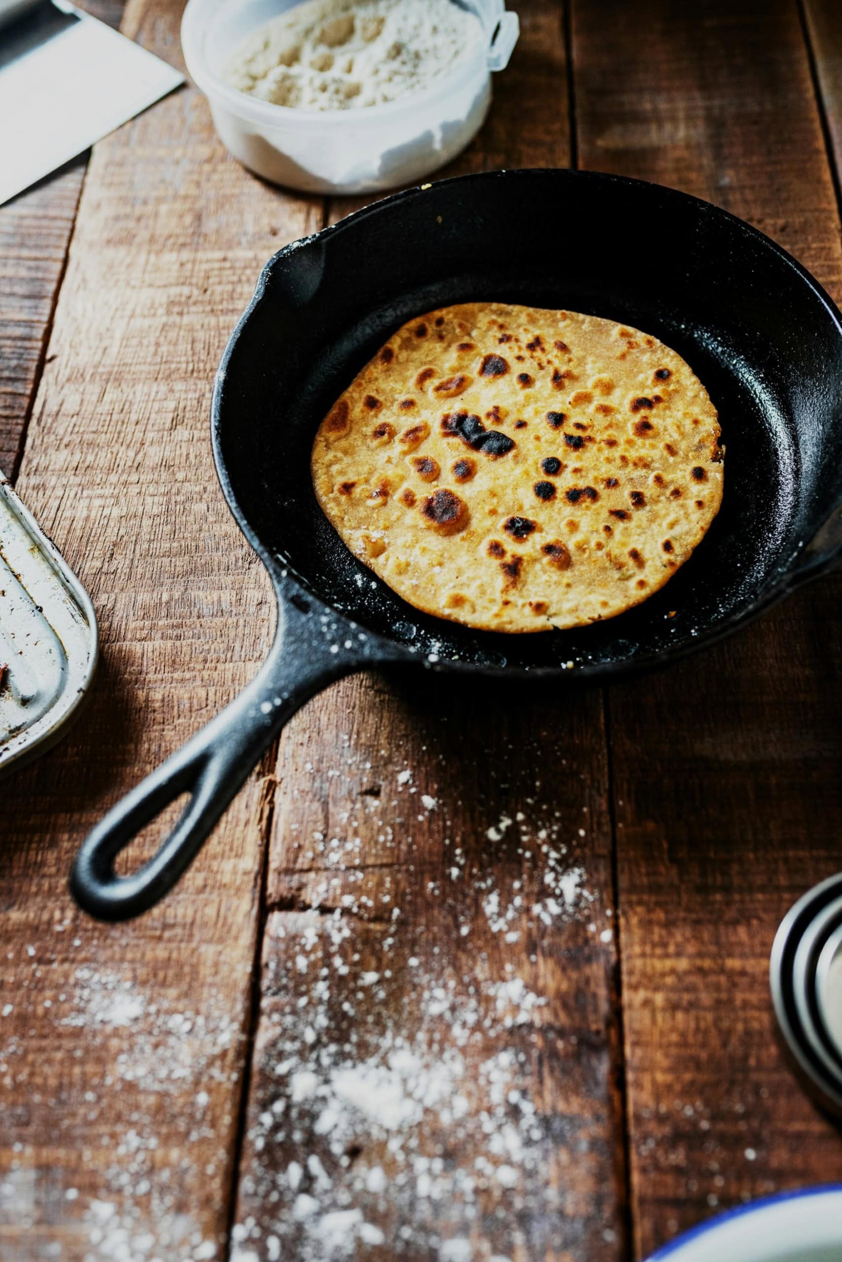 In einer gusseisernen Pfanne liegt ein fertig gegarter Fladen Naan, die Pfanne steht auf einem großen Holzbrett