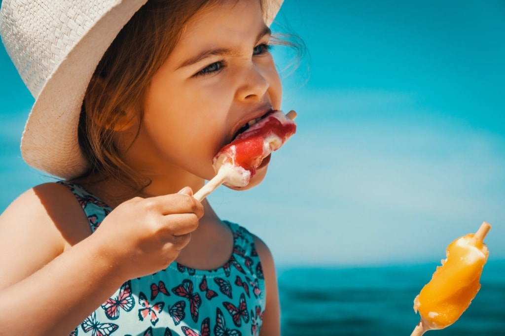 Mädchen mit Sonnenhut isst zwei Eis
